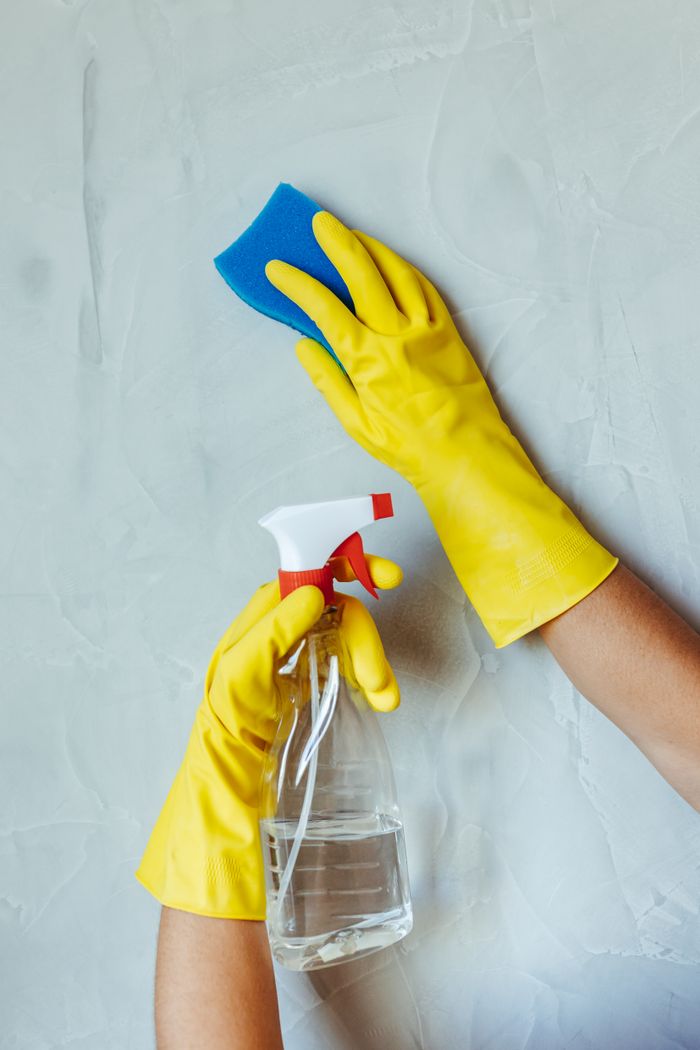 gallery-1 Hands in yellow gloves cleaning wall with sponge and spray bottle.