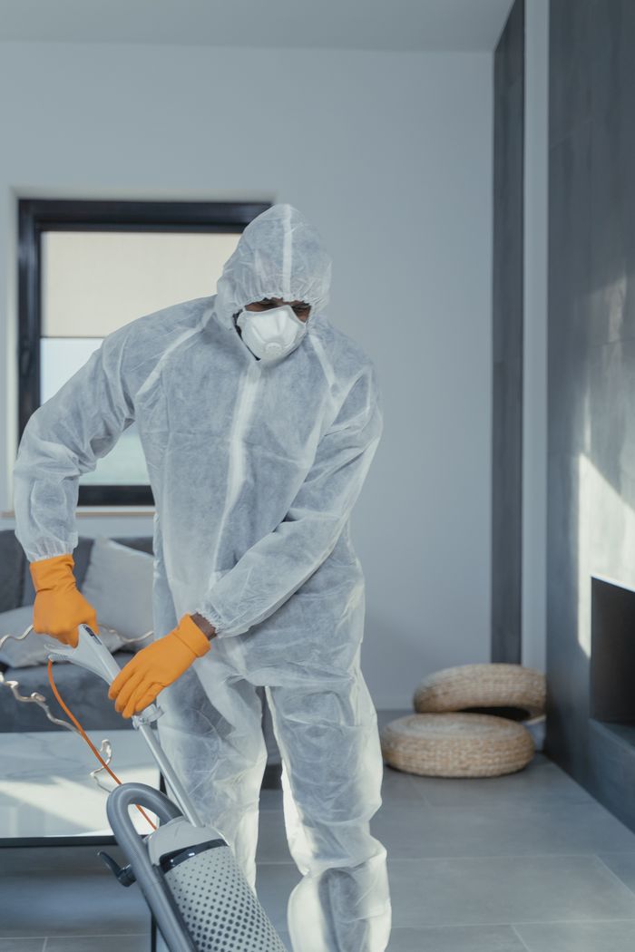 gallery-3 A person in personal protective equipment vacuuming indoors, ensuring a thorough clean.